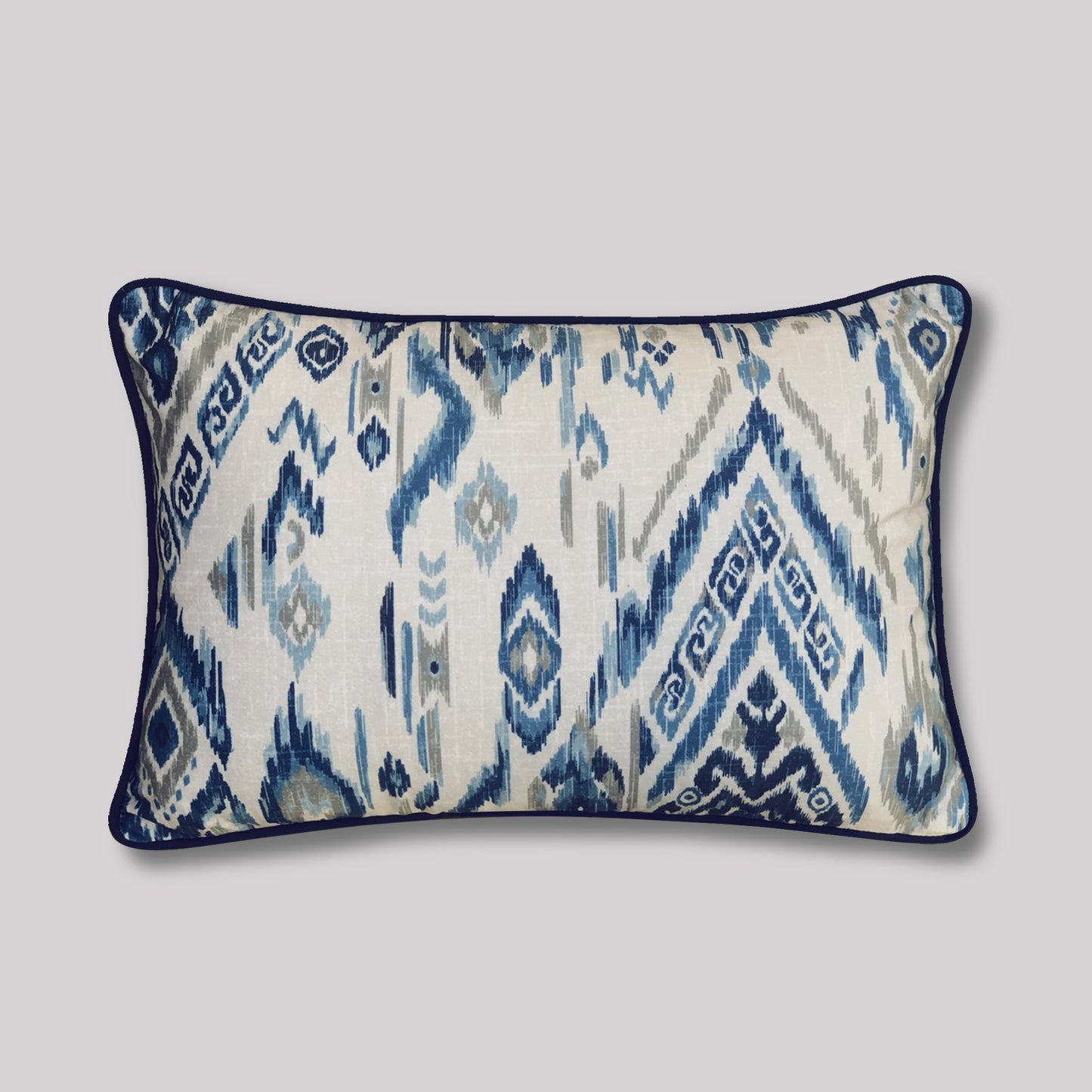 Front view of a 12x18 inch blue and ivory Ikat lumbar cushion cover with geometric diamond pattern and navy piping.