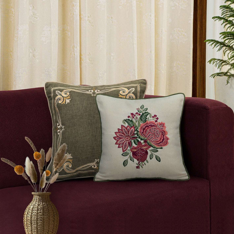Decorative pillows with floral embroidery on a maroon sofa against a beige curtain background.