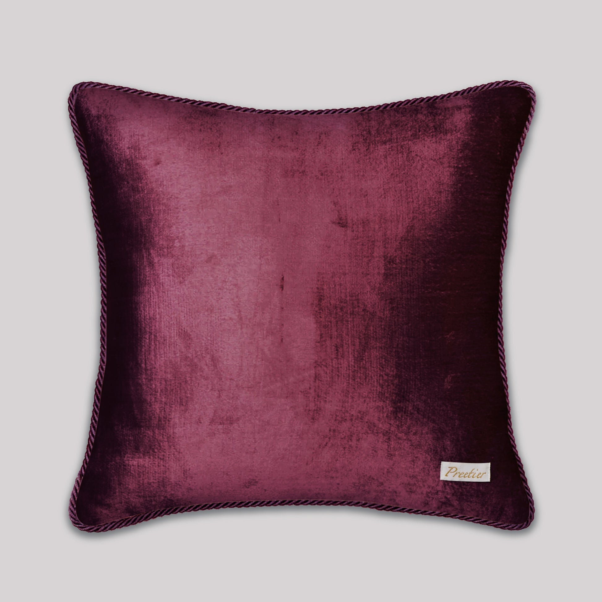 Purple velvet pillow with a brand label on a light gray background
