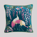 A high-end teal velvet cushion cover featuring detailed silk embroidery of two graceful cranes and cascading pink wisteria, finished with forest green piping.