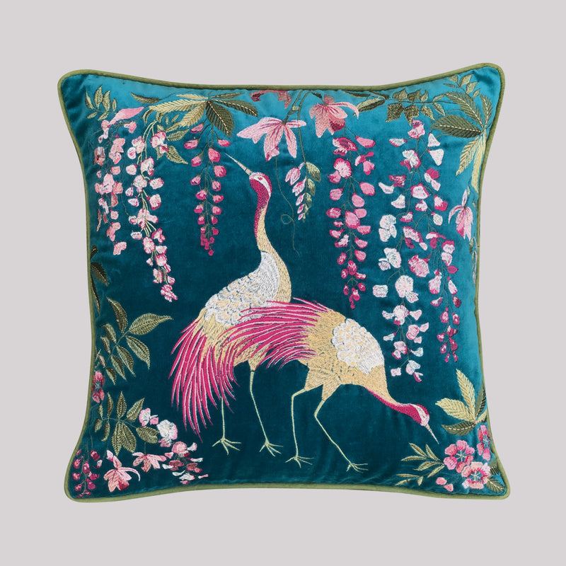 A high-end teal velvet cushion cover featuring detailed silk embroidery of two graceful cranes and cascading pink wisteria, finished with forest green piping.