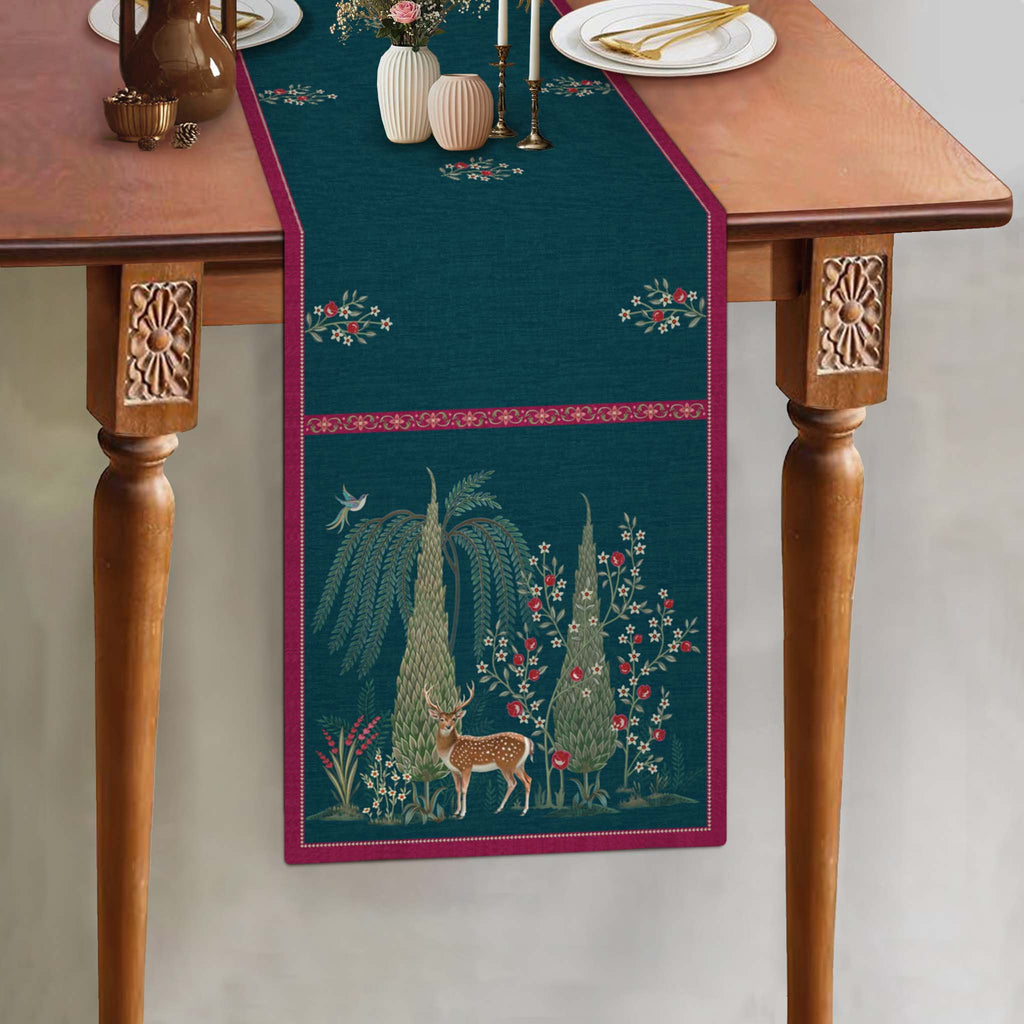 Whispering Grove blue table runner featuring intricate botanical artwork, a graceful deer motif and contrasting berry-pink borders, styled on a wooden dining table.