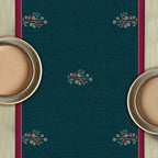 Close-up of the Whispering Grove blue table runner showcasing intricate botanical illustrations, delicate floral accents and a graceful deer motif framed by berry-pink borders.