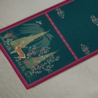Whispering Grove designer table runner in teal blue with nature-inspired artwork and contrasting pink borders, styled with elegant tableware and decorative accents for a refined dining setting.