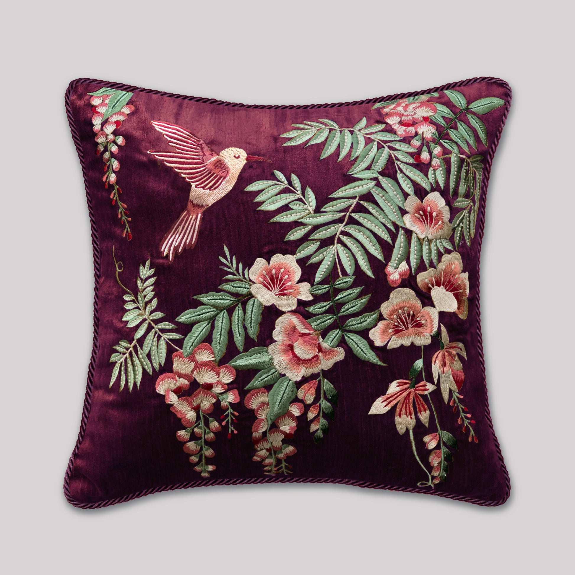 Decorative wine velvet pillow featuring an intricate peach-toned hummingbird hovering over botanical embroidery. The cushion is framed with soft green fringes that give a plush, high-end look. Ideal for modern, floral, and nature-inspired home décor settings.